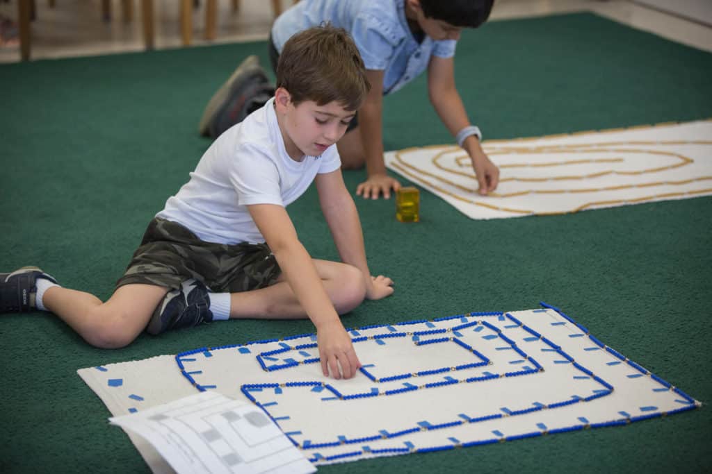 A student makes a maze out of long strings of beads.