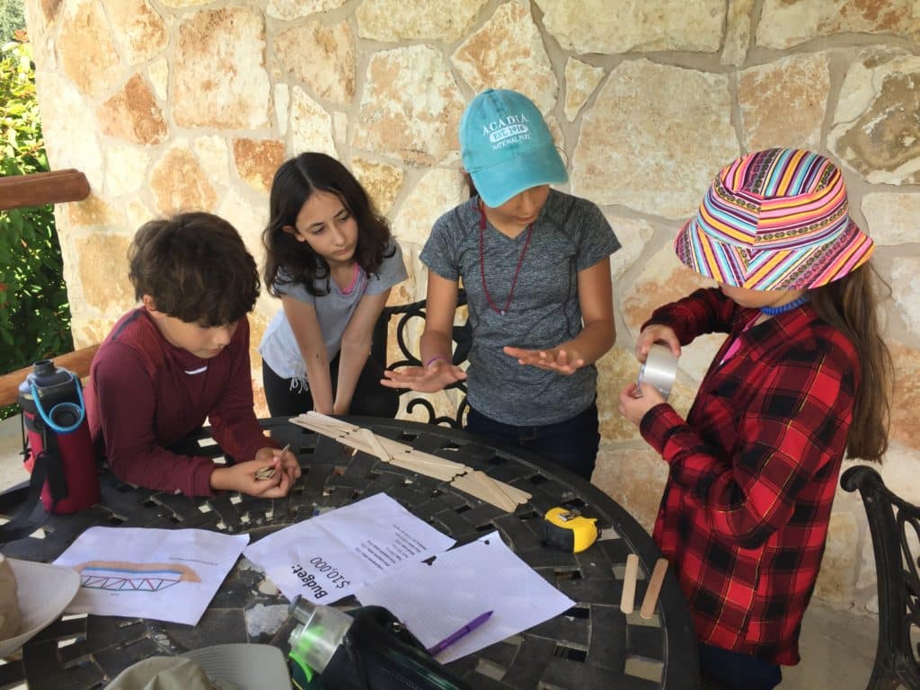 Three students build a small bridge using popsicle sticks and tape.