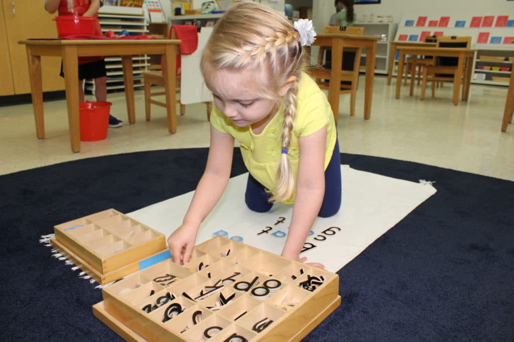 A kid spelling words using large wooden letters.